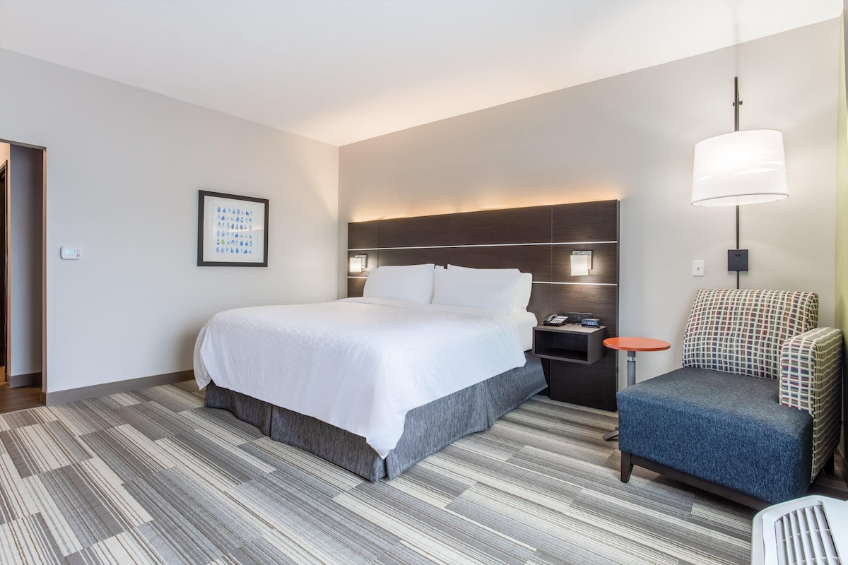 A hotel room with a bed, bedside table, chair, and a wall-mounted lamp.