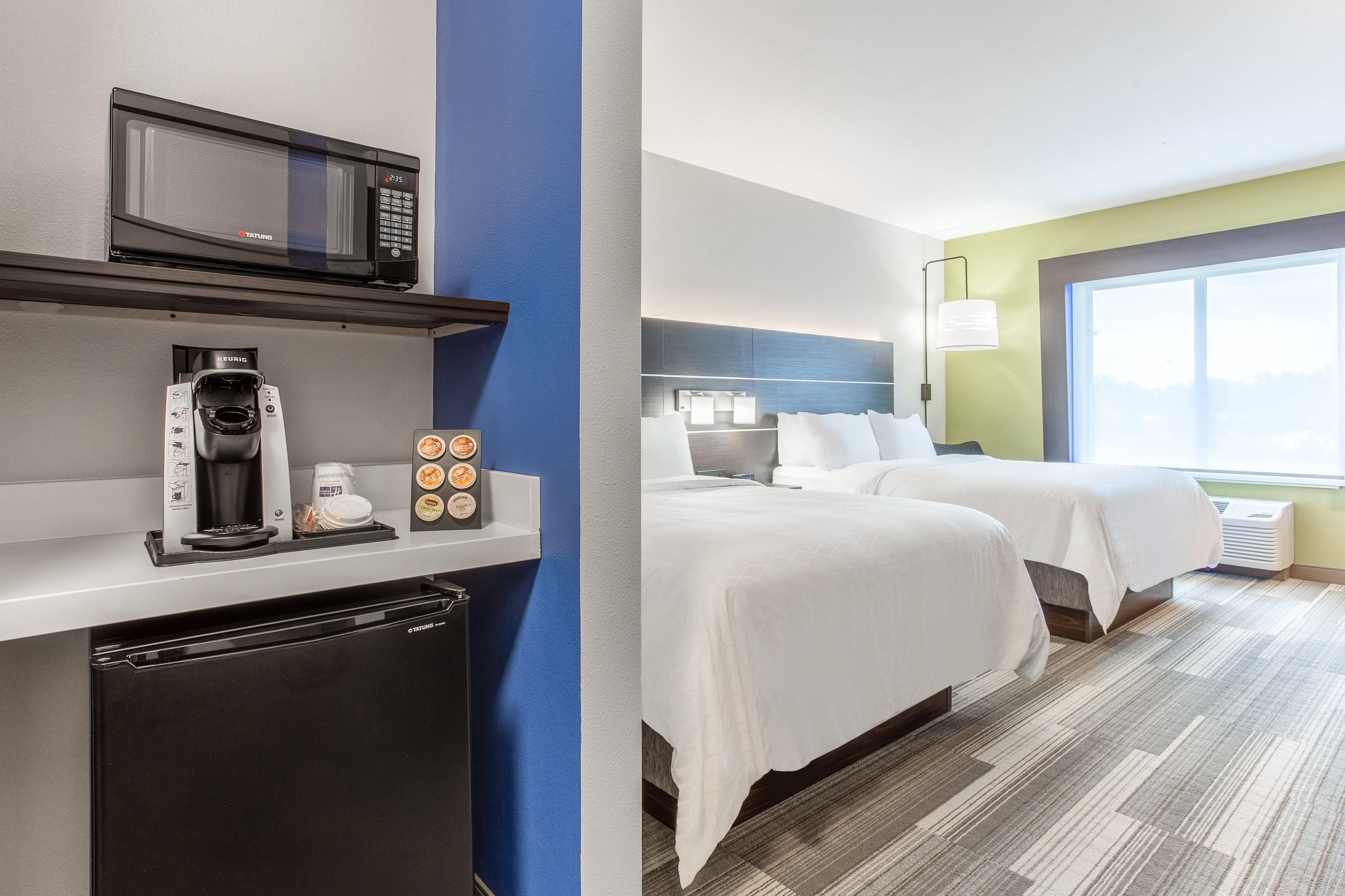 A hotel room with a kitchenette, two beds, a large window, and a view of the city.