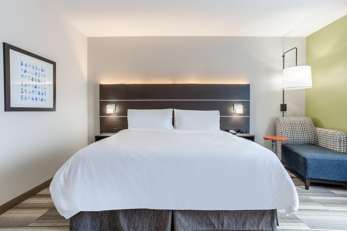 A hotel room with a large bed, bedside tables with lamps, a sofa, and a framed picture on the wall.