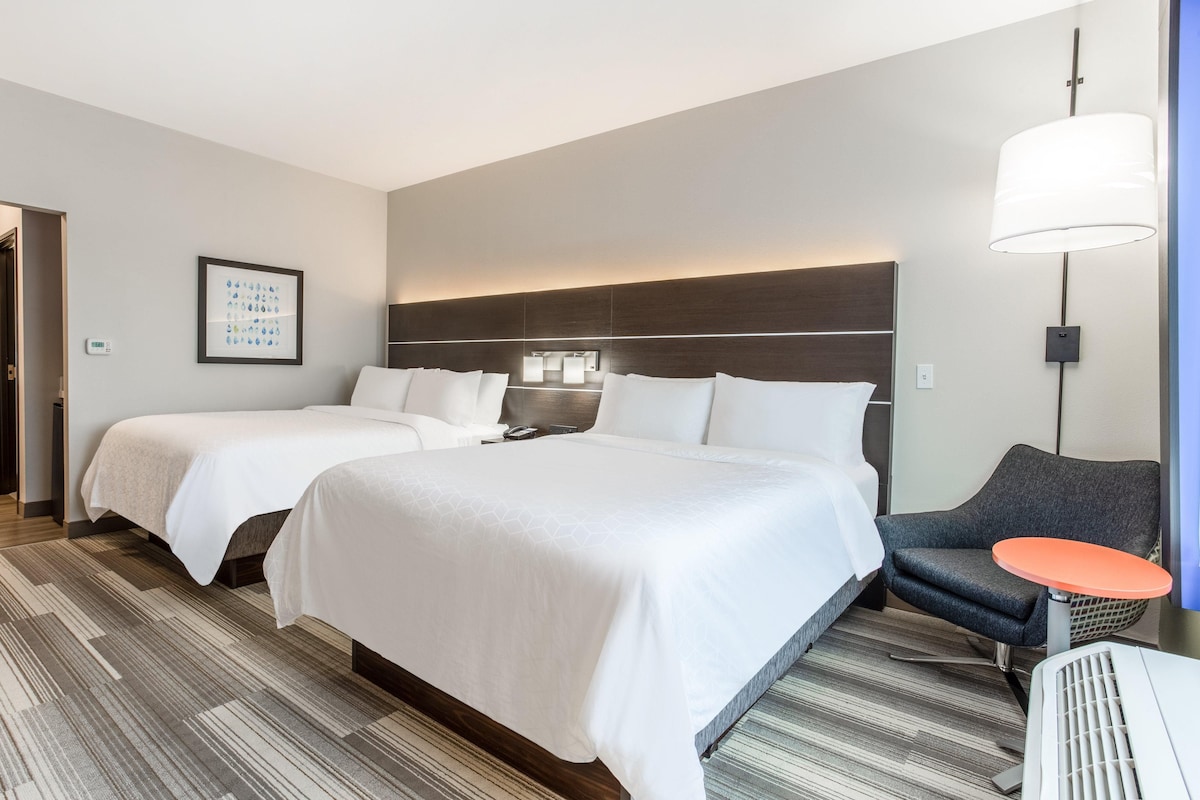 A hotel room with two beds, a desk, a chair, a lamp, and a framed picture on the wall.
