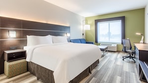 A hotel room with a large bed, a desk, a chair, a lamp, and a window with a view.