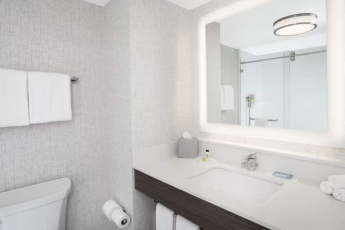 A modern bathroom with a large mirror, white tiles, a dark wood vanity, and a toilet.