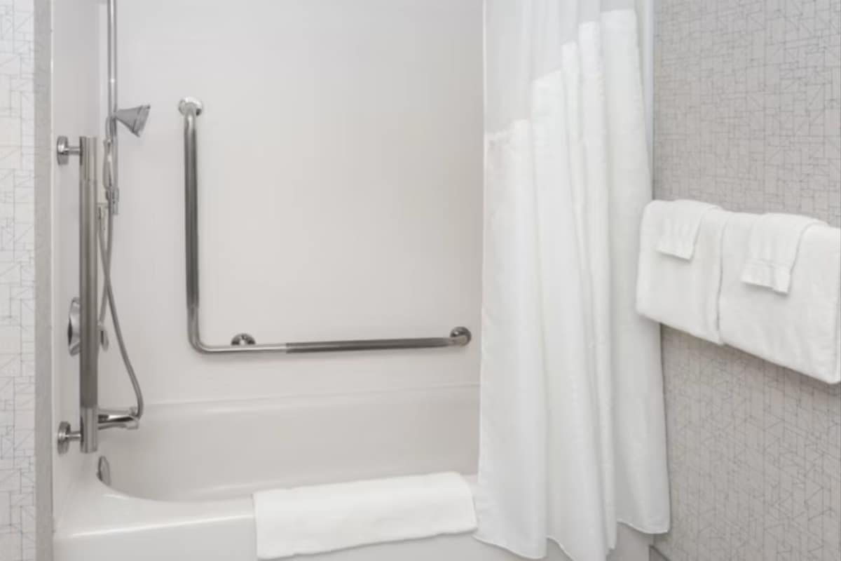 A modern bathroom with a walk-in shower, grab bars, a towel rack, and a shower curtain.