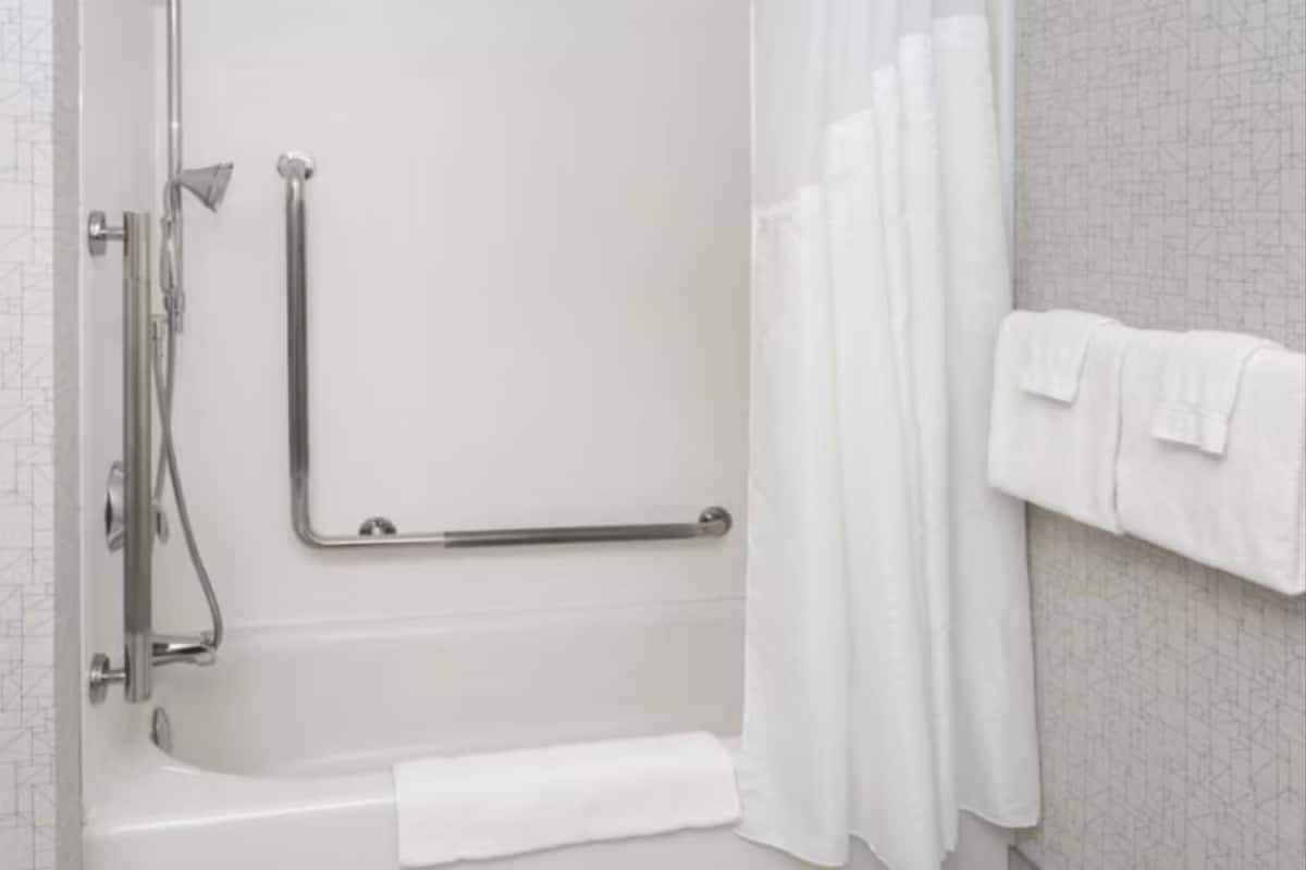 Un baño moderno con ducha a nivel, barras de apoyo, toallero y cortina de ducha.
