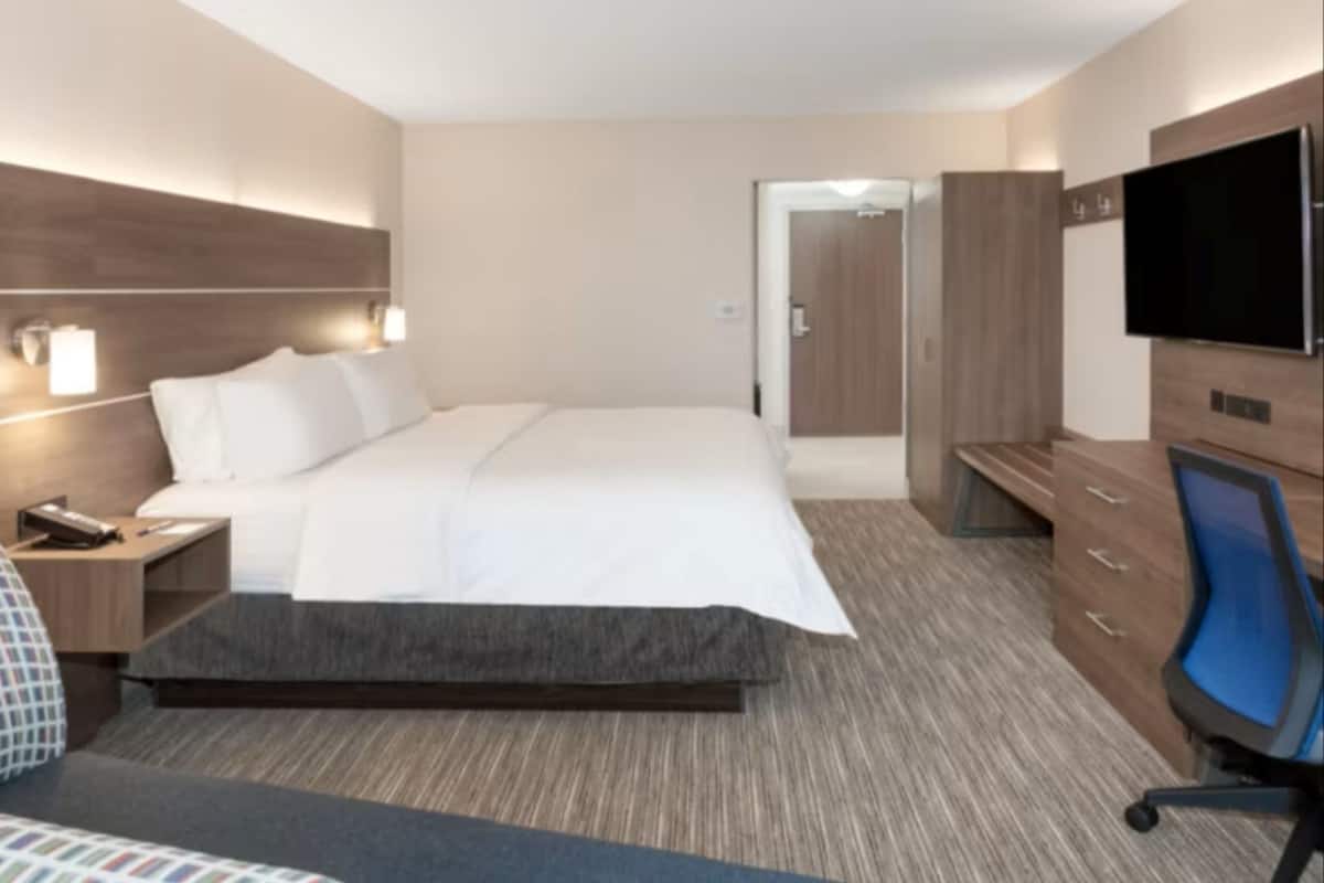 Una habitación de hotel con cama, mesita de noche, lámpara, televisión y armario.