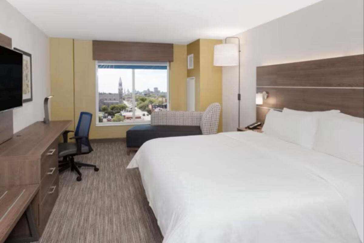 Habitación de hotel con una cama grande, un escritorio con silla, televisor y ventana con vistas a la ciudad.