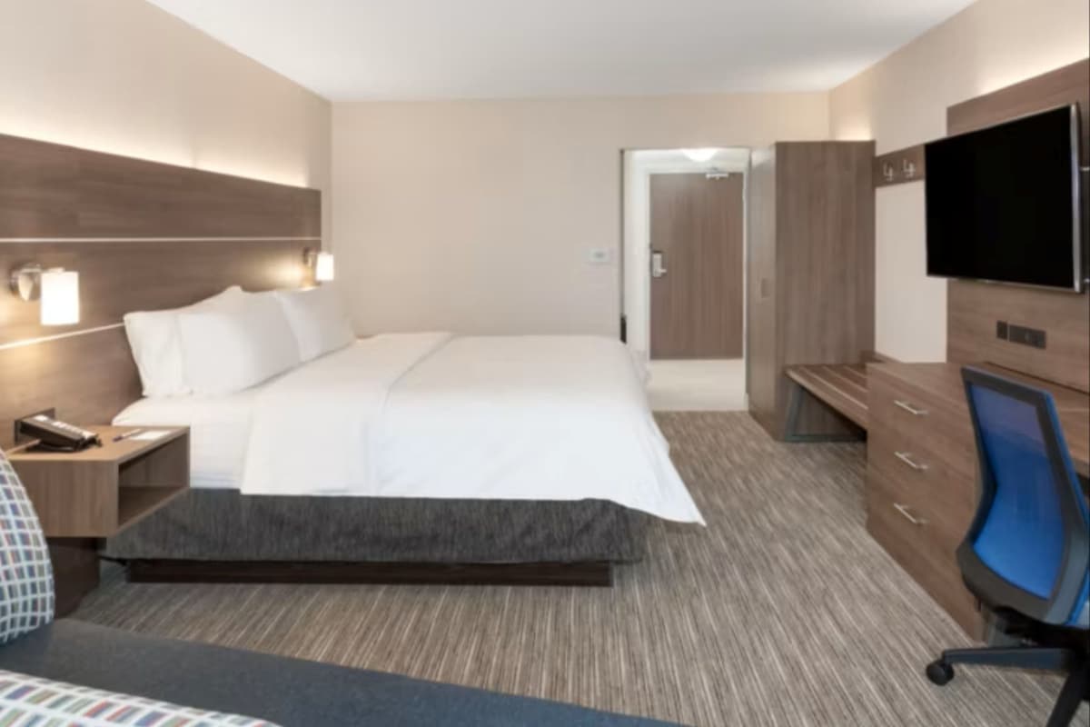 A hotel room with a bed, bedside table, lamp, TV, and a wardrobe.