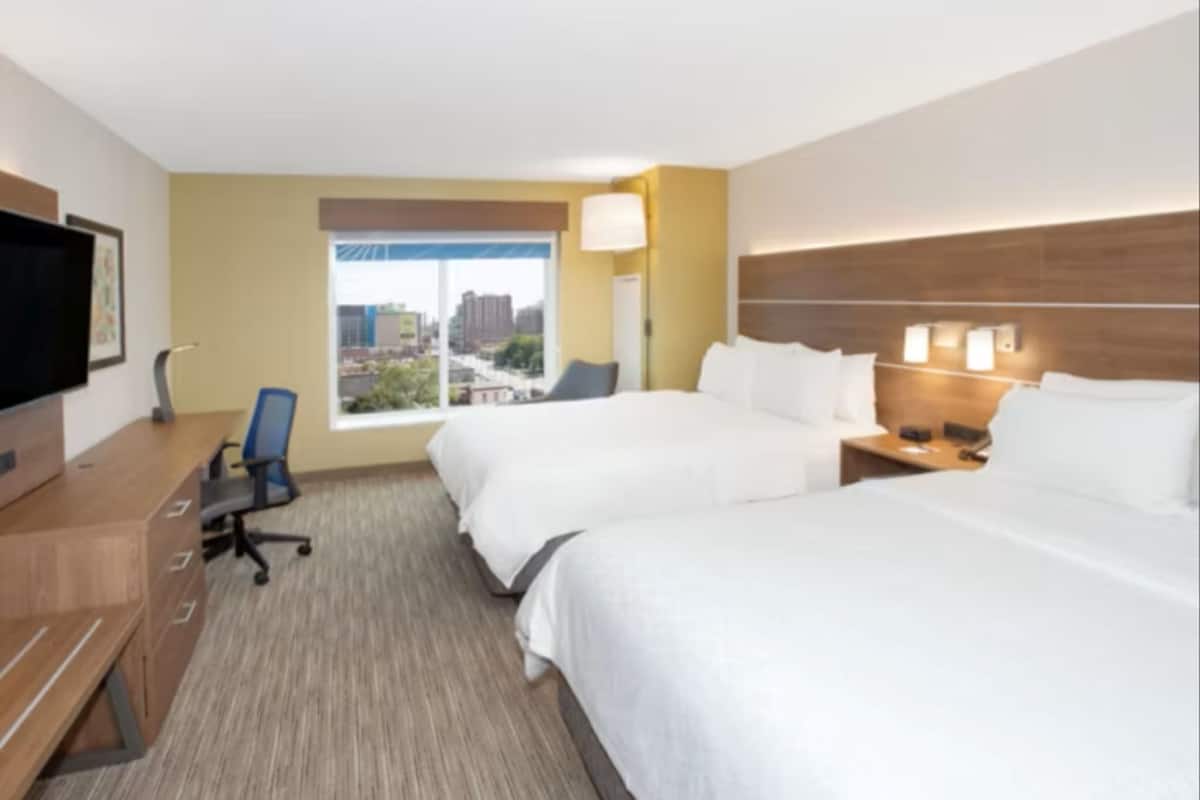 Habitación de hotel con dos camas, un escritorio con silla, televisión y ventana con vista a la ciudad.