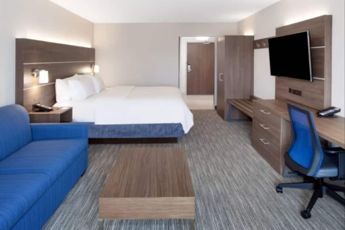 Habitación de hotel con cama, escritorio con silla, televisor y sofá azul.
