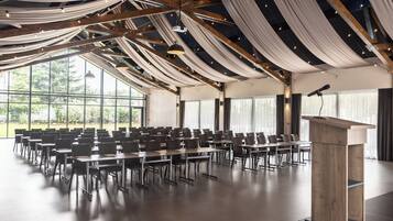 A conference room with rows of tables and chairs, large windows, and a wooden podium.