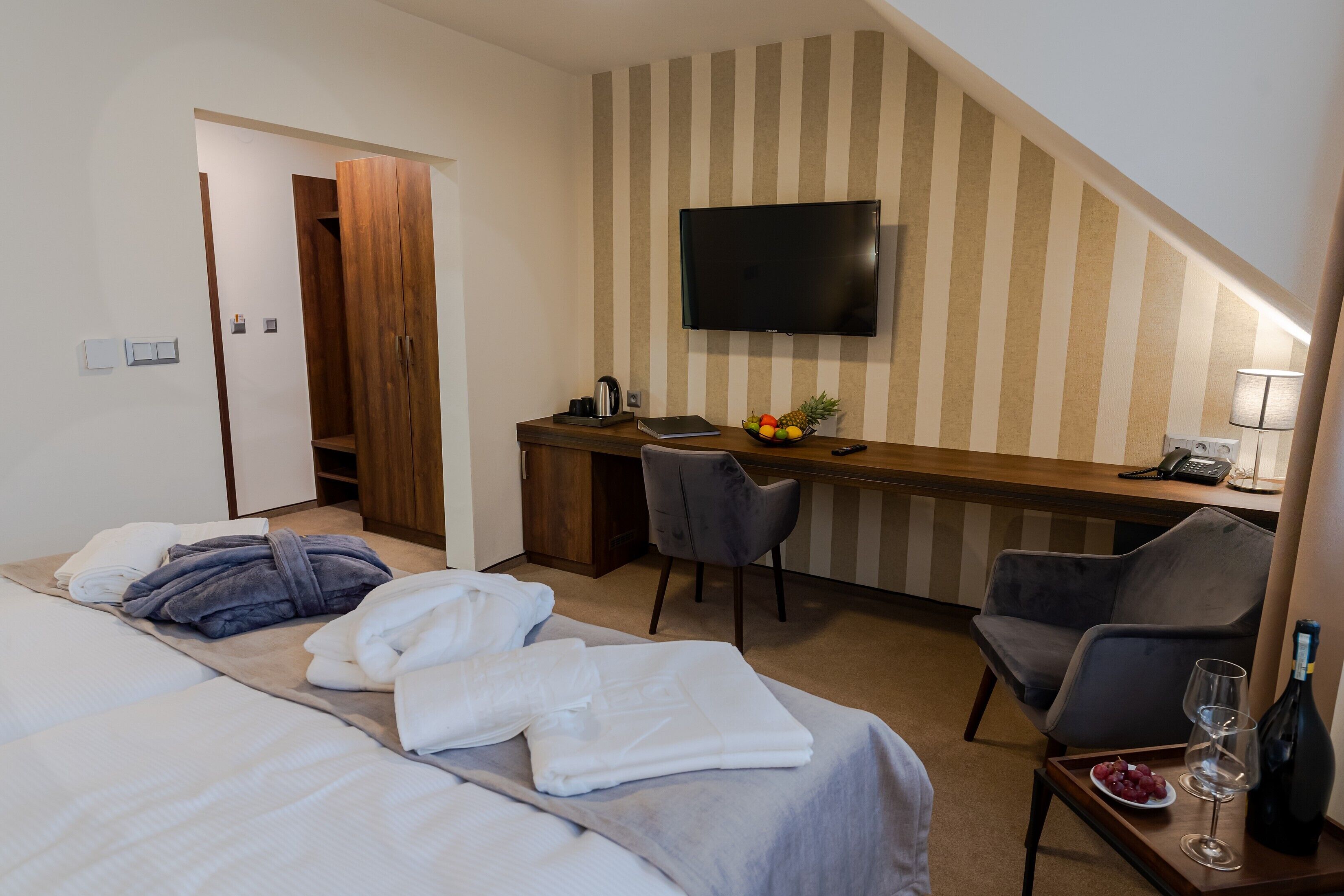 A hotel room with a bed, a desk with a computer, a television, and a small table with a bottle and glasses.