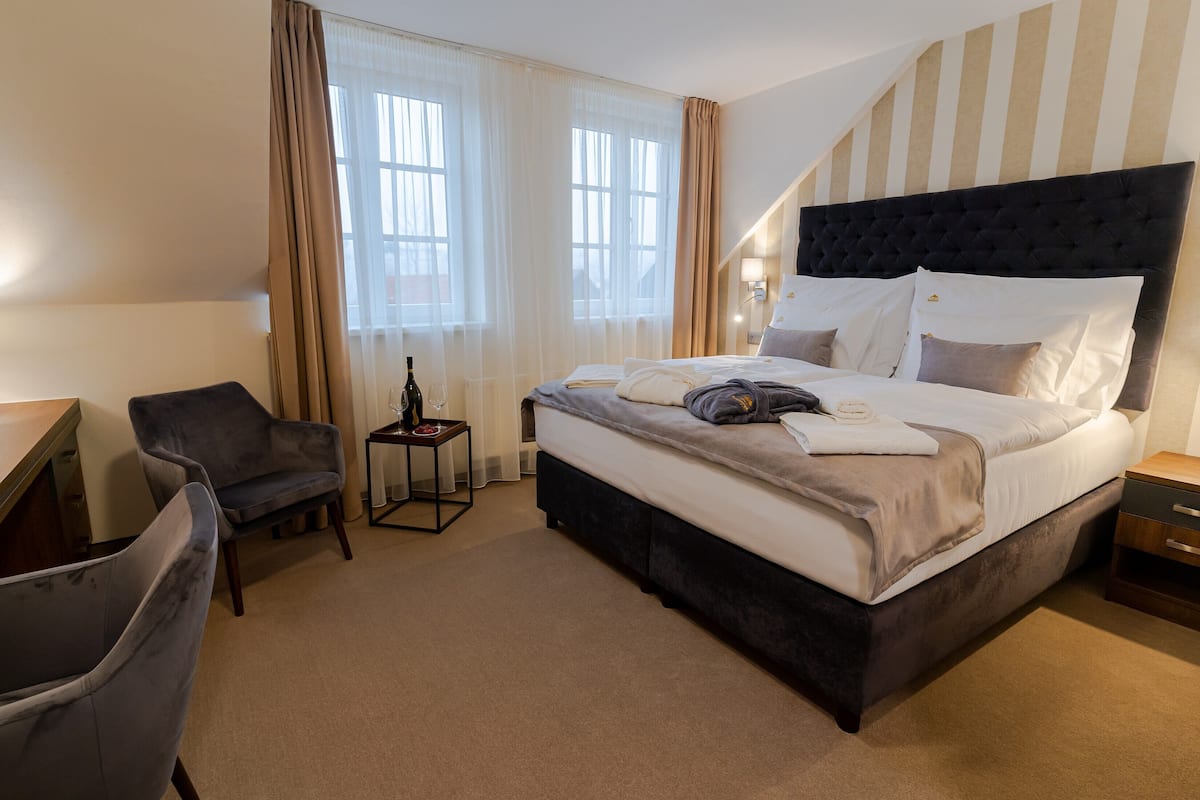 Une chambre d’hôtel avec un grand lit, une chaise, une petite table avec une bouteille et des rideaux aux fenêtres.