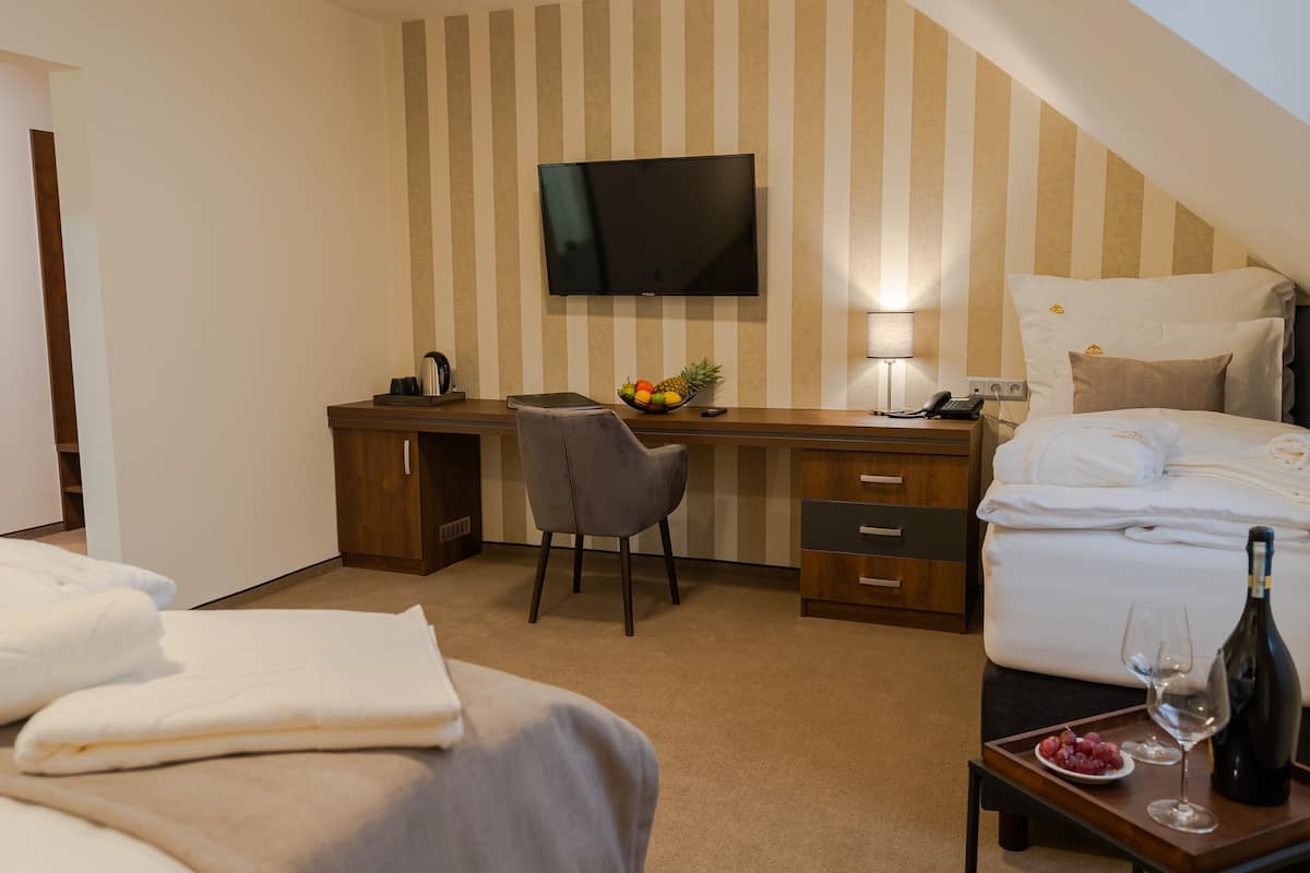 Une chambre d’hôtel comprenant un lit, un bureau, une chaise, une télévision, une table de chevet avec une bouteille et un verre, et un panier de fruits.