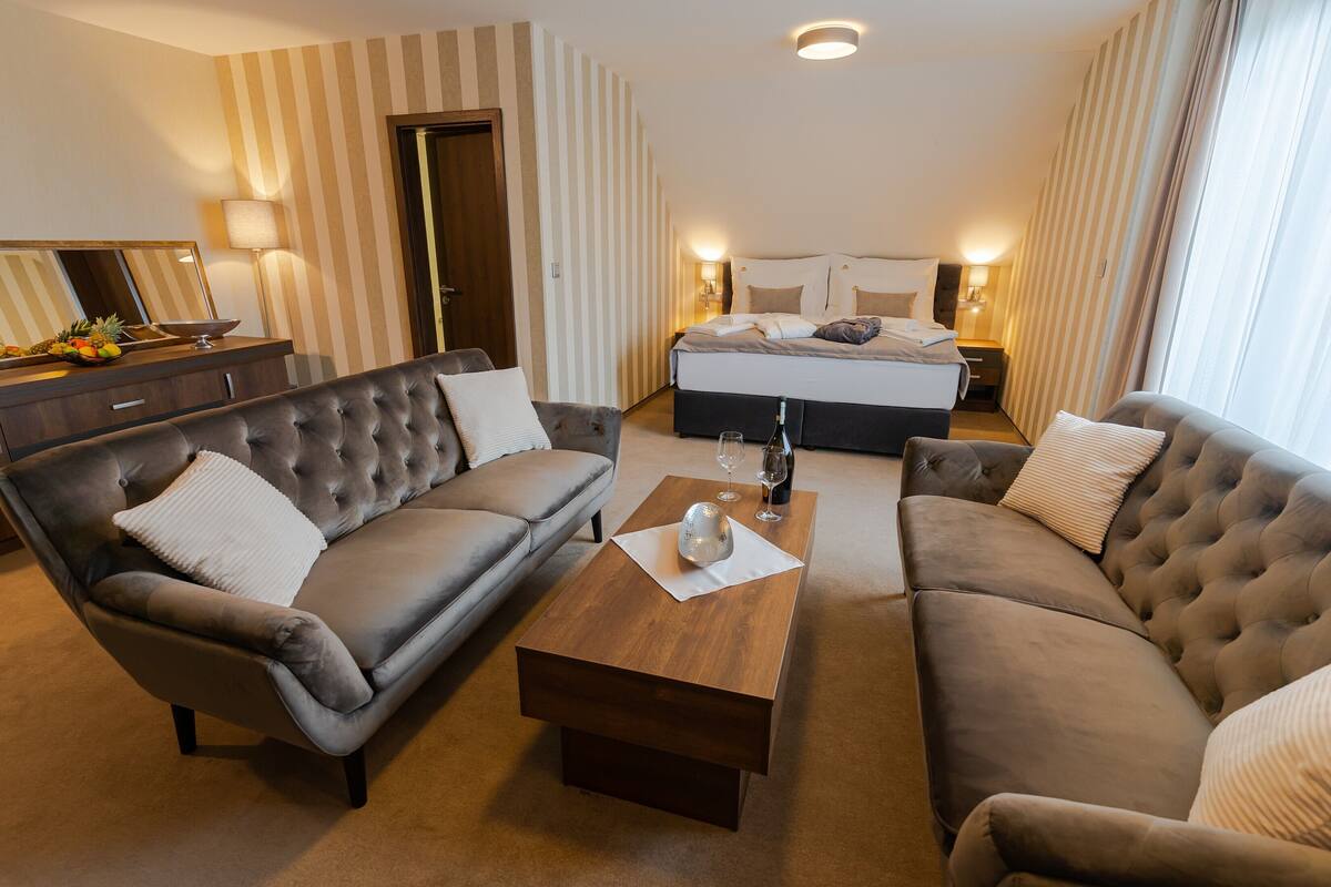 Une chambre d’hôtel avec un grand lit, deux canapés, une table basse en bois et un miroir.