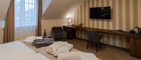 A hotel room with a large bed, a desk with a computer, a TV, and a window with curtains.