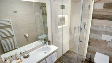 Un baño moderno con ducha envuelta en vidrio, un espejo grande y un lavabo blanco con artículos de aseo.
