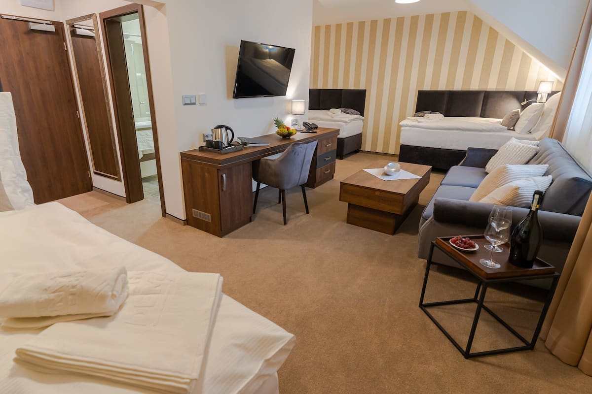 Une chambre d’hôtel comprenant un lit, un bureau avec une chaise, un canapé, une télévision et une petite table avec une bouteille et des verres.