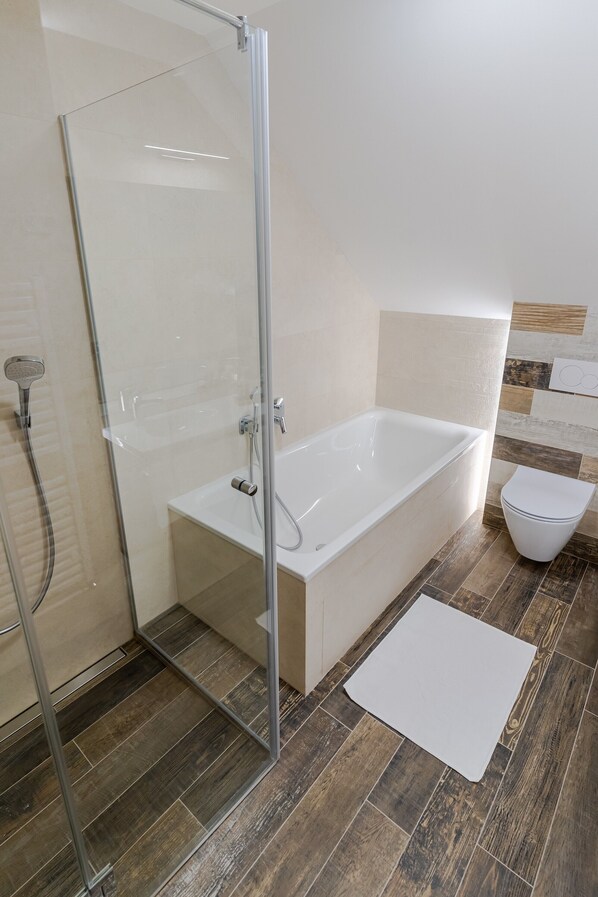 A bathroom with a glass shower enclosure, a white bathtub, and a toilet.