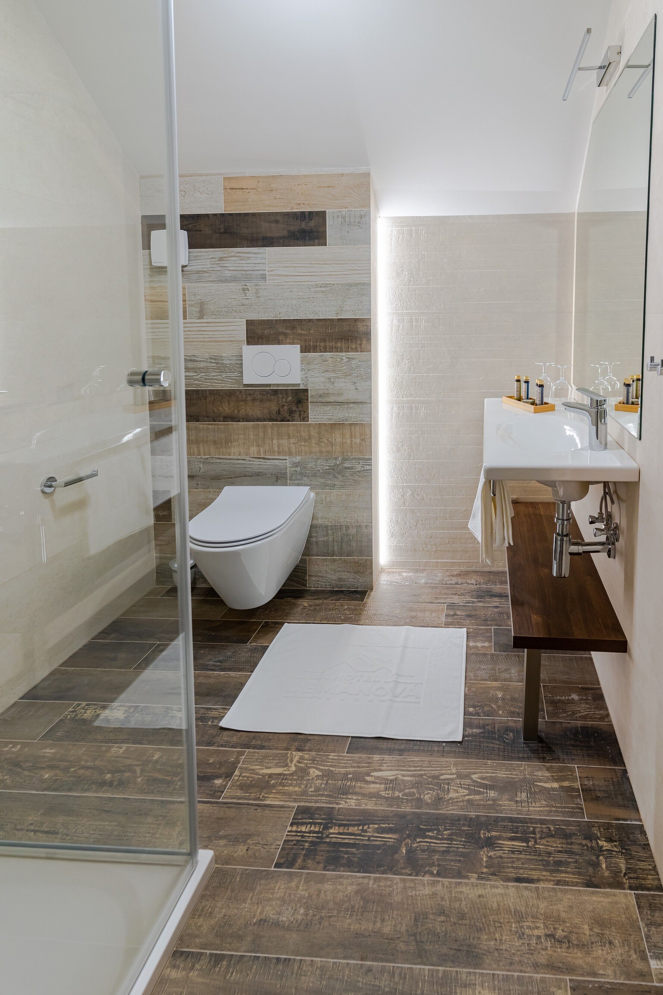 A modern bathroom with a glass shower enclosure, a white toilet, and a wooden vanity with a mirror.