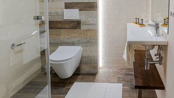 A modern bathroom with a glass shower enclosure, a white toilet, and a wooden vanity with a mirror.