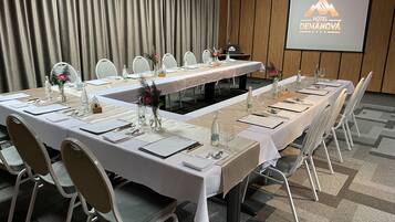 A conference room with a long table set for a meeting, white chairs, and a projector screen displaying the hotel name.
