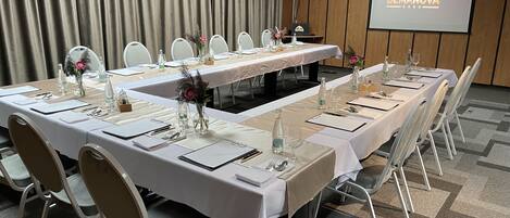 A conference room with a long table set for a meeting, white chairs, and a projector screen displaying the hotel name.