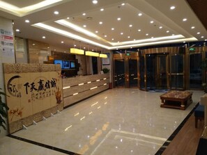 A hotel lobby with a reception desk, a digital screen, a wooden reception counter, a coffee table, and a glass elevator. - Greentree Inn Beijing Tongzhou District Yujiawu Techonology Park Express Hotel (Tongzhou)