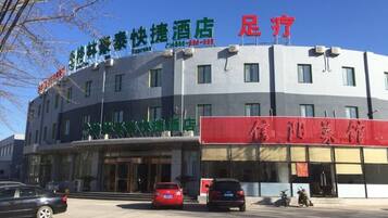 A hotel with a signboard displaying Chinese characters, a red signboard with more Chinese characters, and a few parked cars in front.