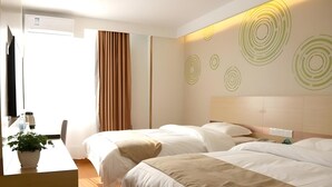 Ein Hotelzimmer mit zwei Betten, einem Schreibtisch, einem Stuhl, einer Zimmerpflanze und einer Wand mit kreisförmigen Mustern.