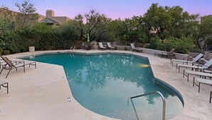 Une piscine avec des chaises longues et un espace patio, entourée d’arbres et avec un bâtiment en arrière-plan.