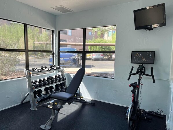 A gym with a bench, dumbbells, a stationary bike, and a TV on the wall.