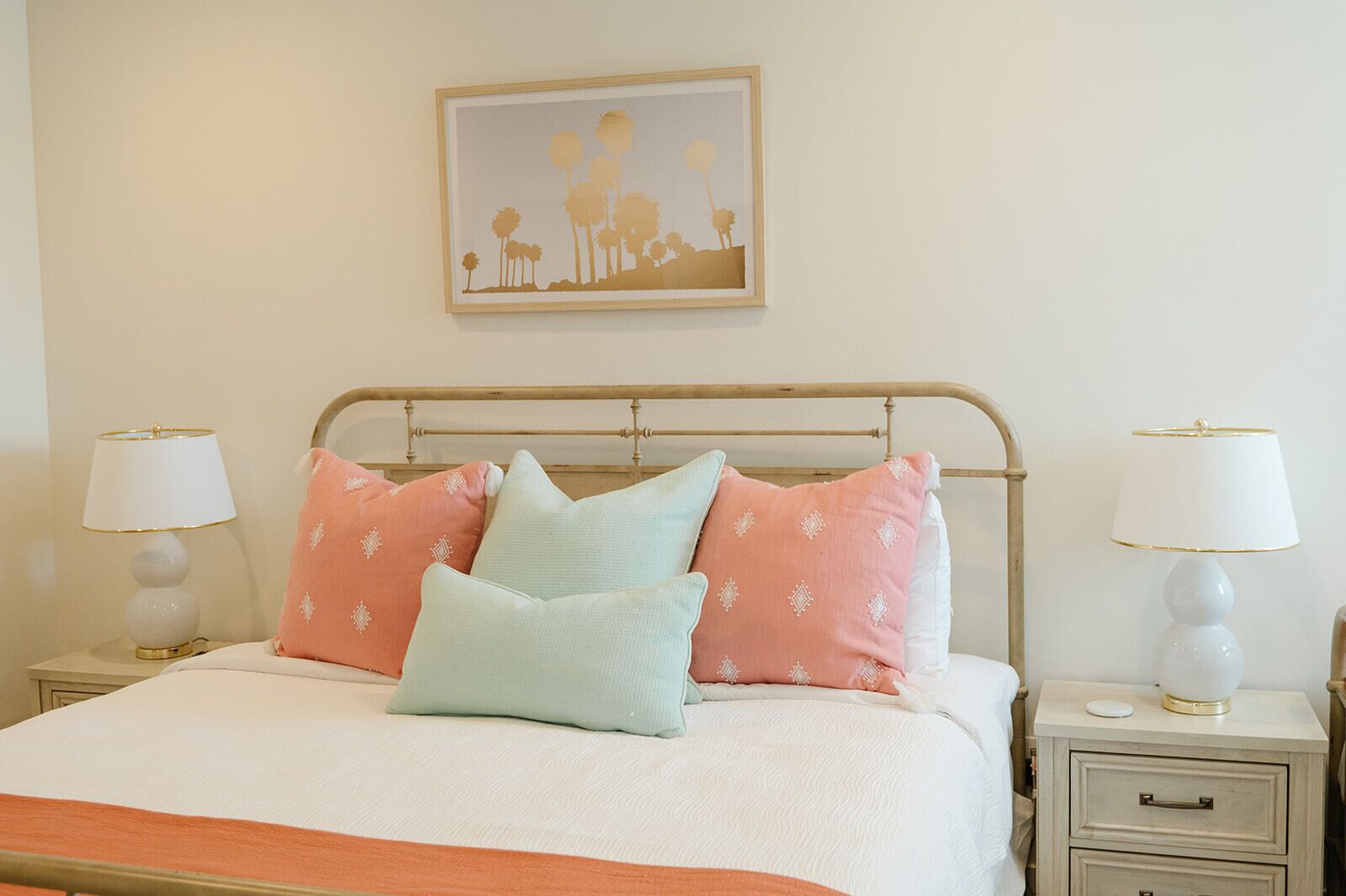 A neatly made bed with a white and orange bedspread, flanked by two bedside tables with lamps, and a framed picture above the bed.