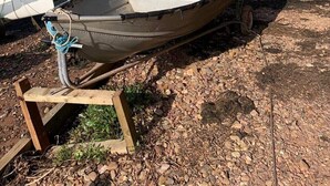 Una pequeña embarcación en una orilla rocosa, con una vista despejada del agua y barcos a lo lejos.