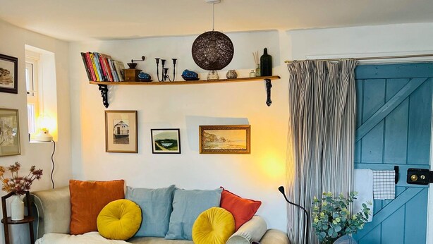 Una sala de estar acogedora con un sofá, sillones y una mesita de centro. Se observan estanterías, cuadros enmarcados y una cortina azul.
