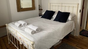 Una cama bien hecha con ropa de cama blanca y dos almohadas oscuras, un cabecero de madera y un espejo en la pared.