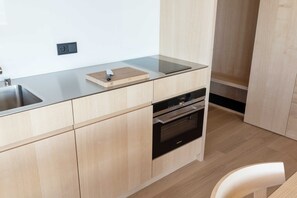 A modern kitchen with a stainless steel sink, wooden countertop, built-in oven, and light wood cabinetry.
