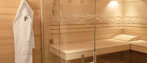 A sauna with a glass partition, a towel rack, and a bench.