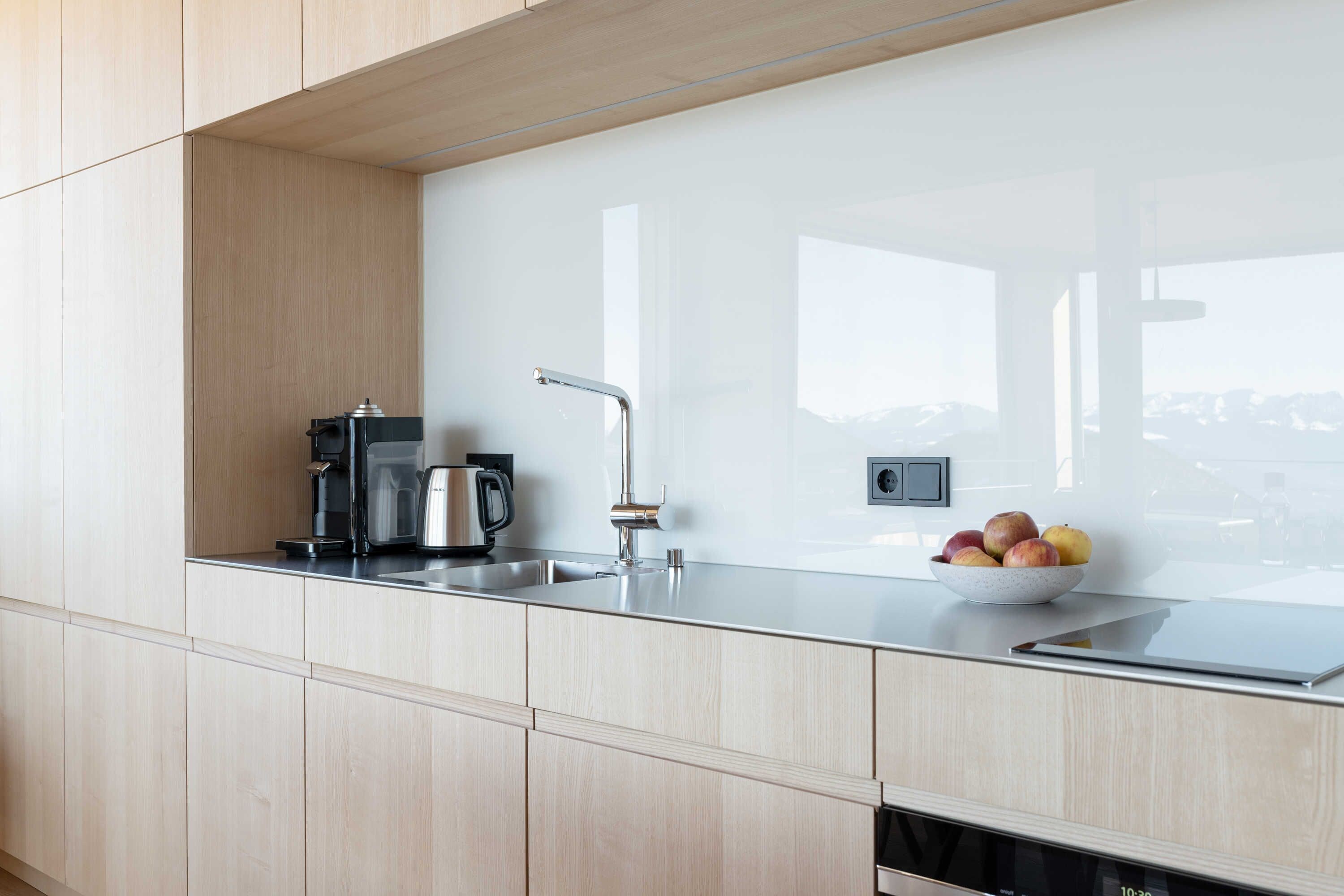A modern kitchen with a stainless steel sink, a kettle, and a bowl of fruit.