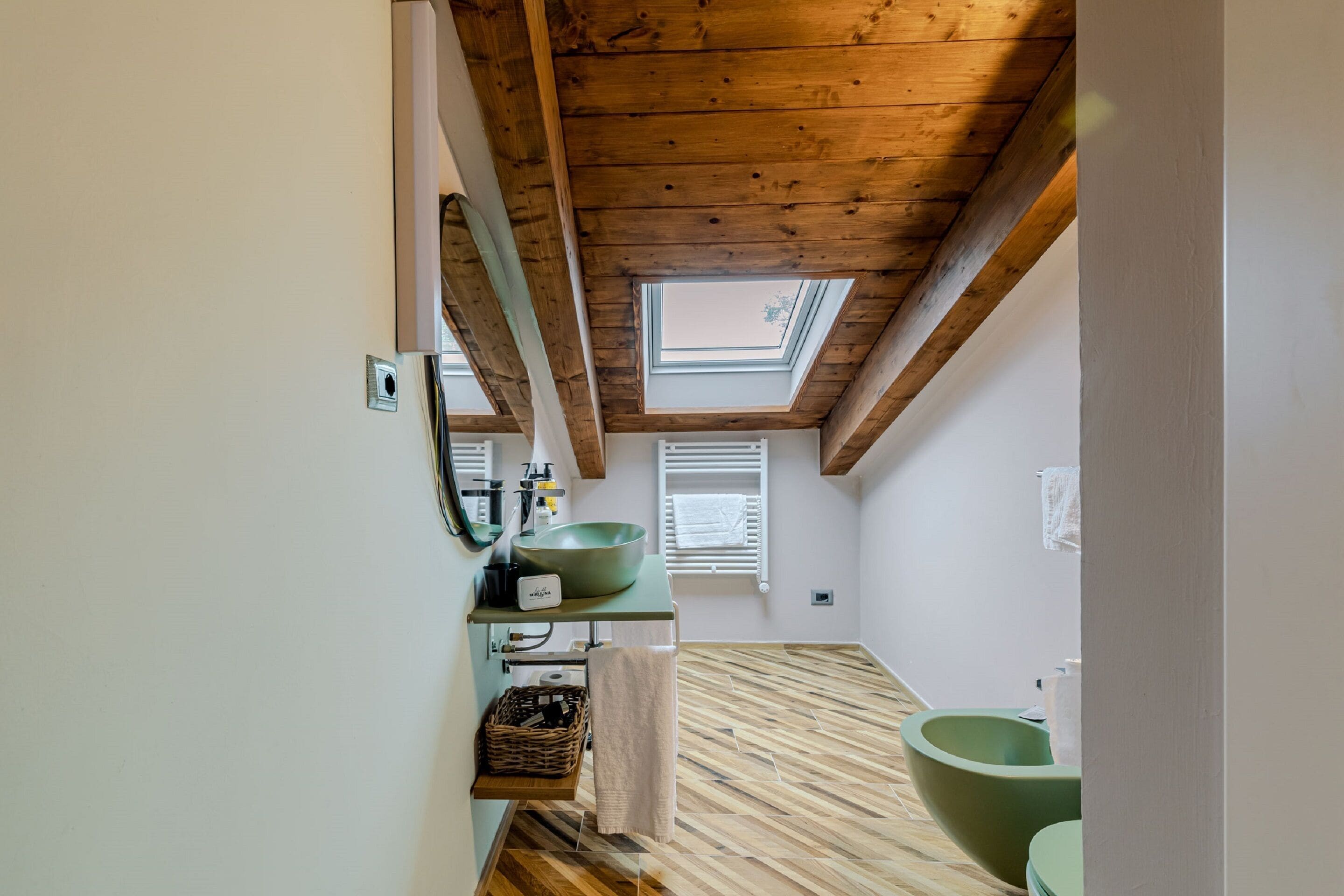 Un baño con tragaluz, un lavabo verde grande y suelo de madera.