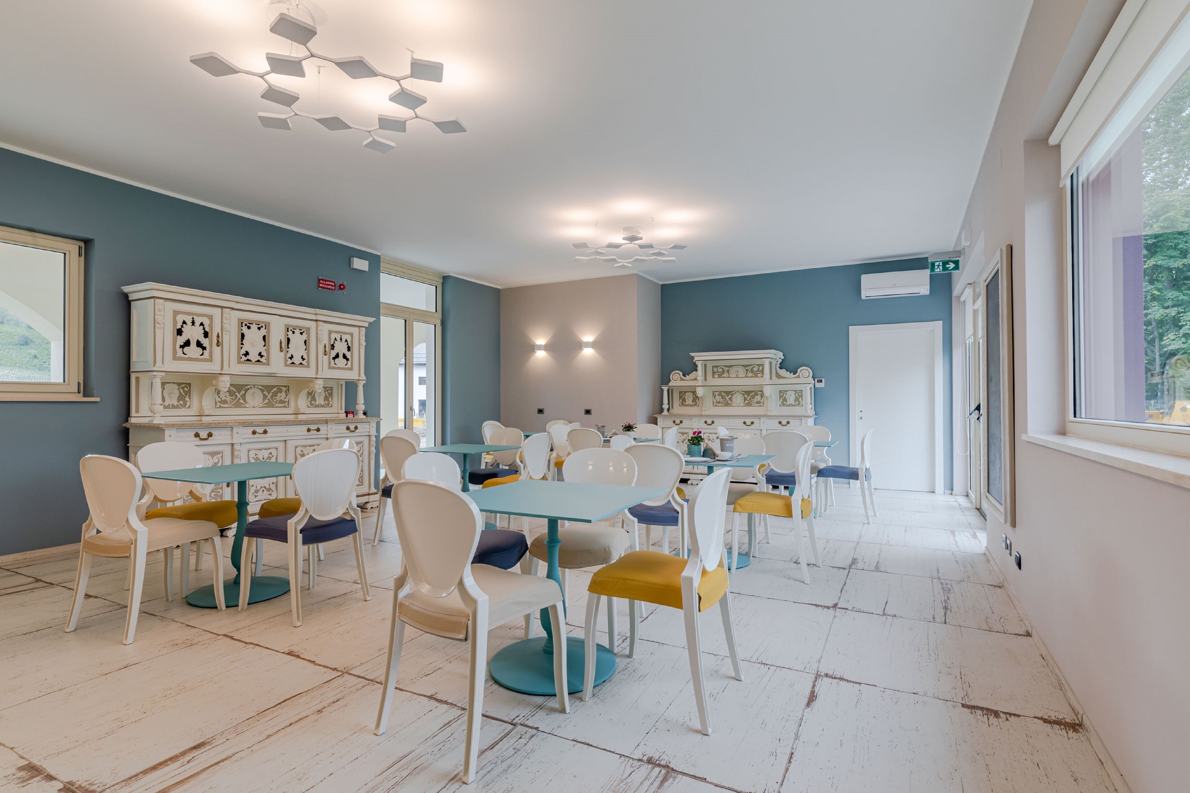 Un amplio comedor con sillas blancas y amarillas, mesas color turquesa y armarios blancos decorativos.