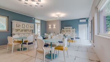 Un amplio comedor con sillas blancas y amarillas, mesas color turquesa y armarios blancos decorativos.