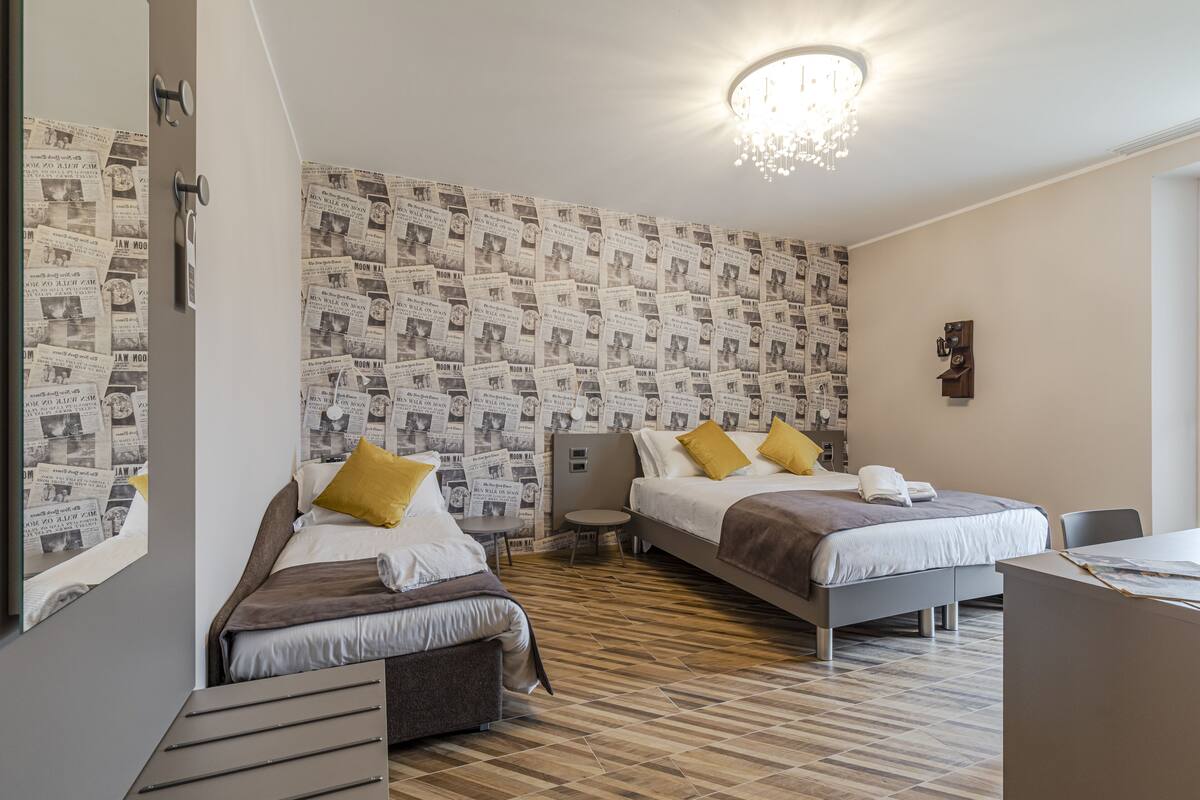 Habitación de hotel con dos camas, un escritorio, una silla, una mesita y un espejo.