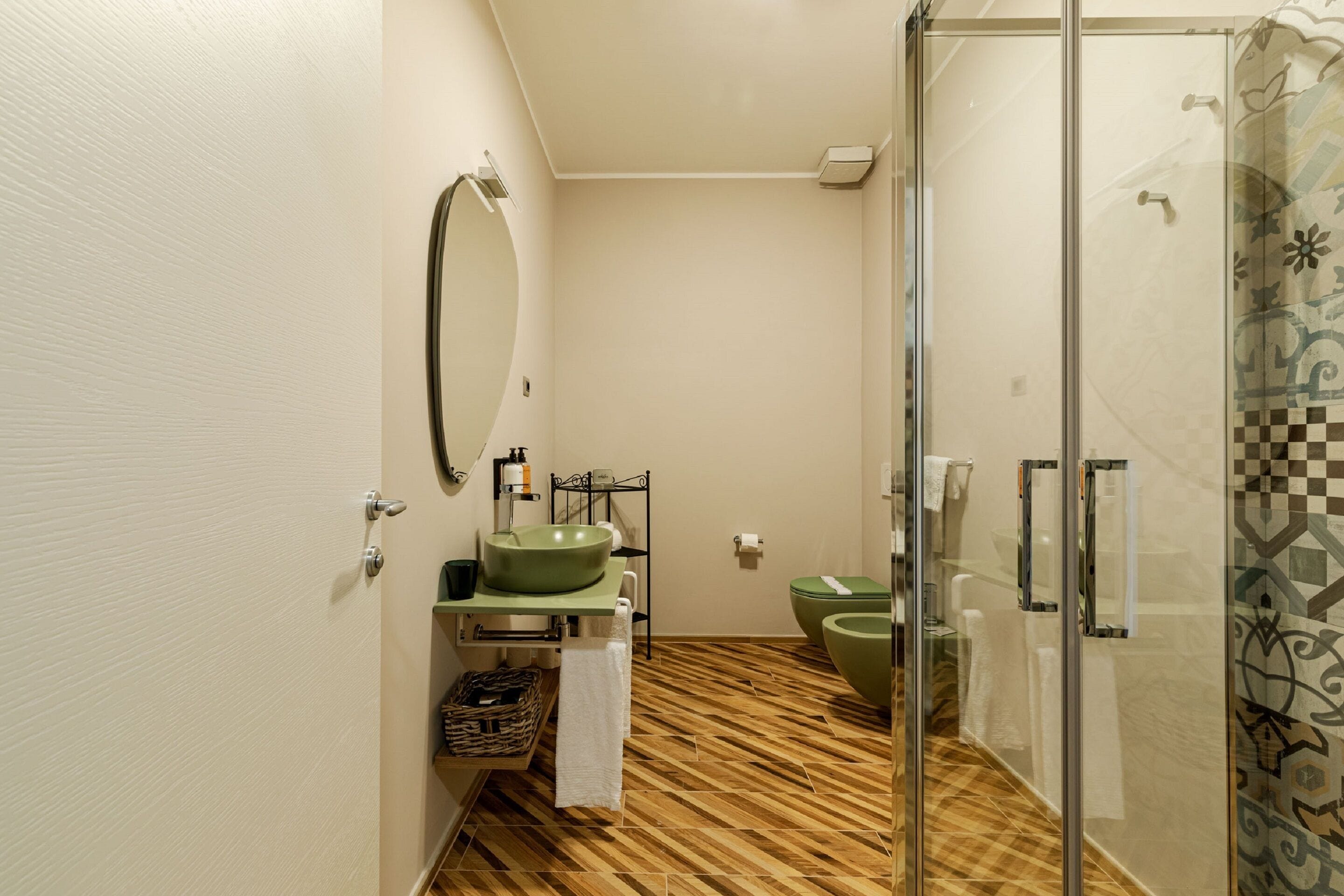 Une salle de bain avec un plancher en bois, un lavabo vert et une cabine de douche en verre.