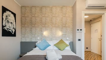 Ein modernes Hotelzimmer mit einem gemusterten Kopfteil, einem Bett mit zwei Kissen, einem ordentlich gefalteten weißen Handtuch und einem gerahmten Kunstwerk an der Wand.