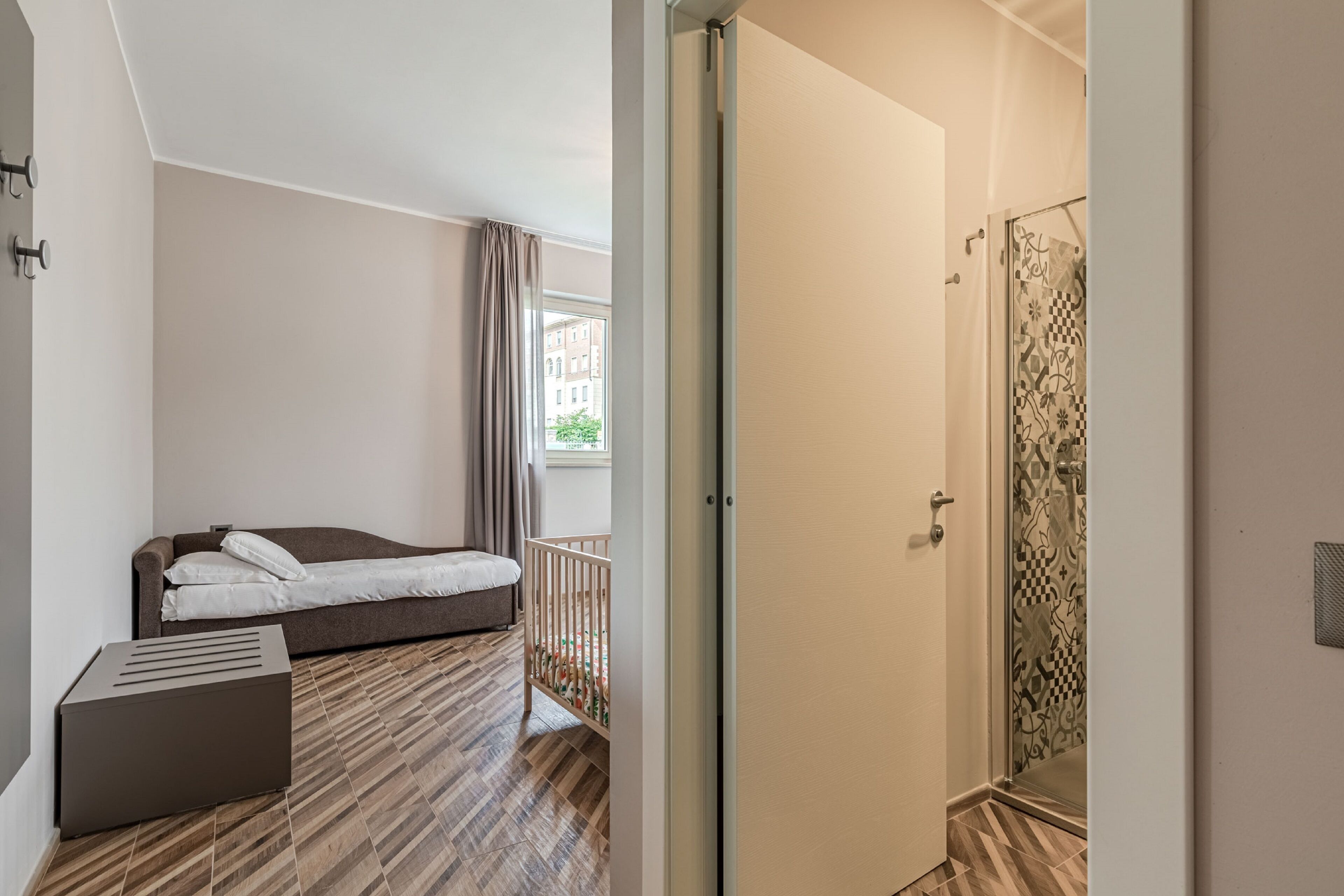 Een slaapkamer met een bed, een klein tafeltje, een ledikant en een douche met betegelde muren.