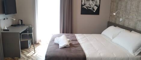 A hotel room with a bed, a desk, a chair, a television, and a poster on the wall.