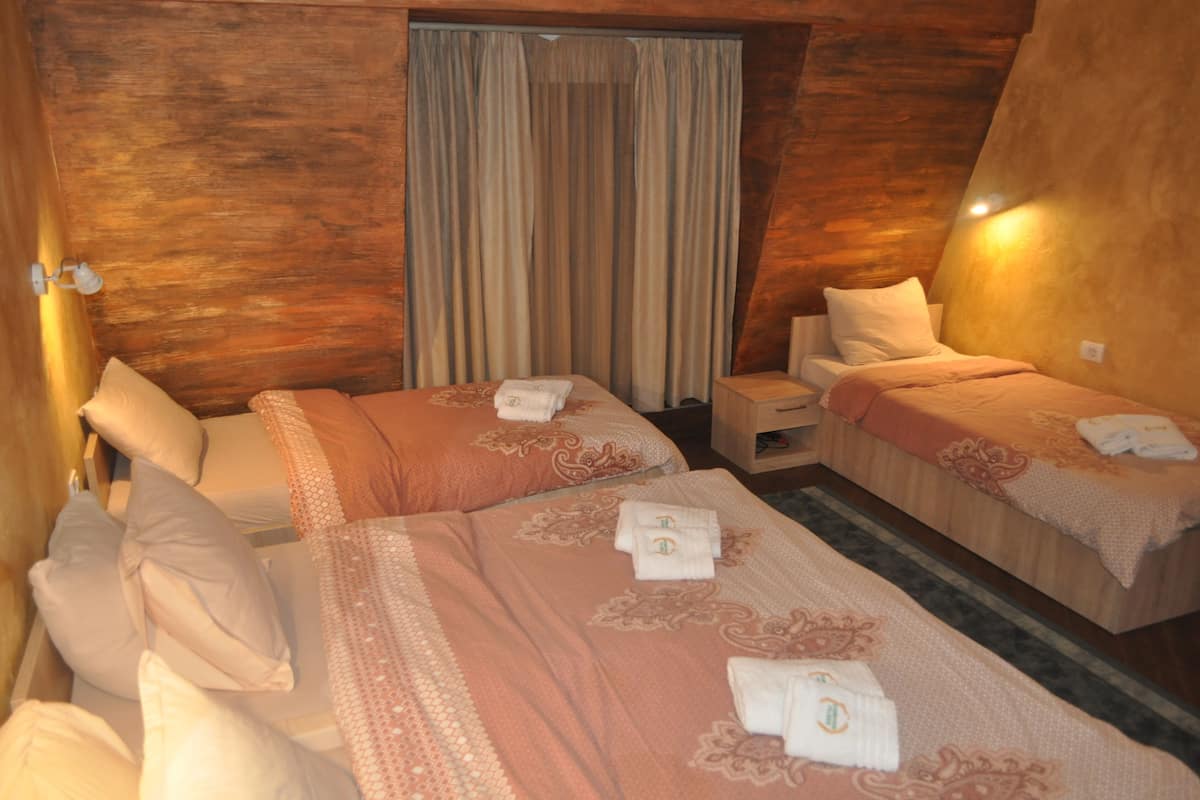 A hotel room with two beds, each with a matching headboard and pillow. There is a nightstand between the beds, and a window with curtains.