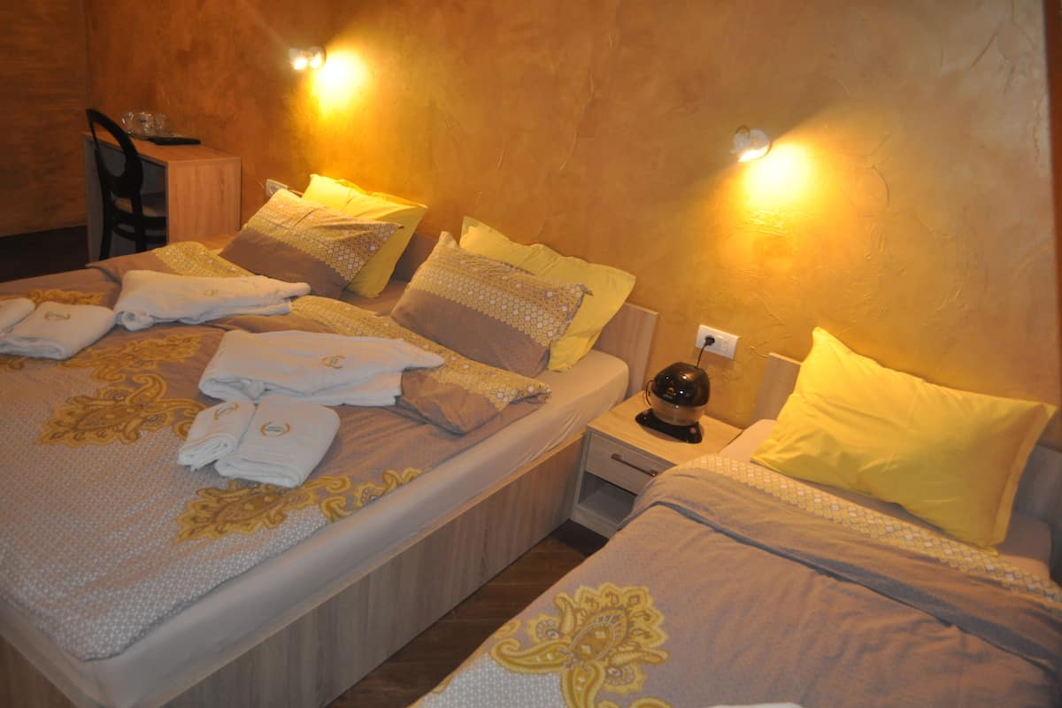 A hotel room with two beds, each with neatly folded towels and decorative pillows. There is a small table with a chair and a nightstand with a lamp.