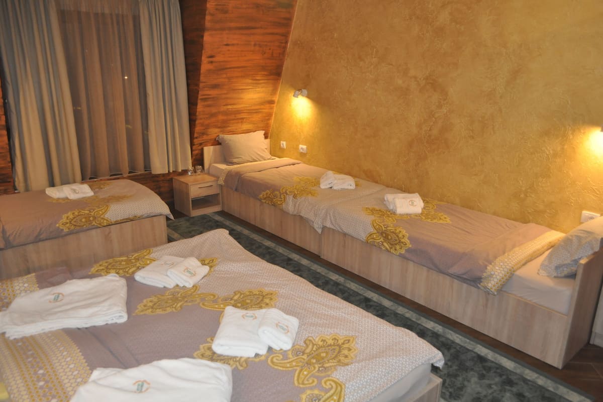 A hotel room with two single beds, a nightstand, and a large window with curtains.