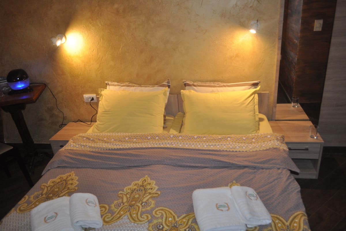A hotel room with a bed, two bedside lamps, a nightstand, and a wall-mounted light fixture.